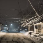 Snow-covered street during an ice storm, with power lines and branches weighed down by ice, illustrating potential hazards during power outages.